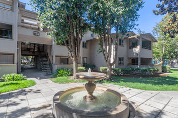 A fountain in the middle of a courtyard surrounded by trees and buildings at The Woods Apartments, San Jose